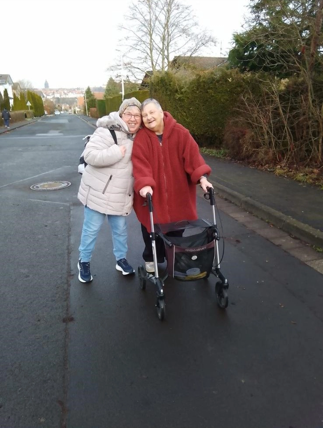 Soziale Teilhabe Kilian und Partner - sozialpädagogische Hilfe - zwei gemeinsam lächelnde Personen auf einer Straße, wobei eine Person eine Mobilitätshilfe benutzt