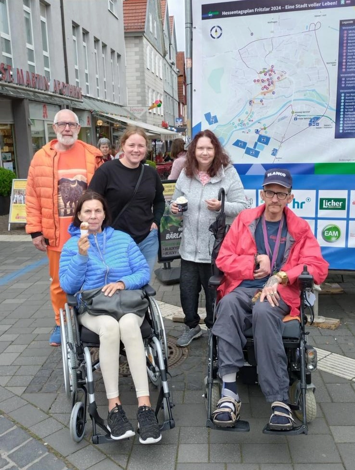 Soziale Teilhabe Kilian und Partner – sozialpädagogische Hilfe – eine Gruppe von fünf Personen, die in einer Fußgängerzone für ein Foto posieren, wobei zwei Personen im Rollstuhl sitzen