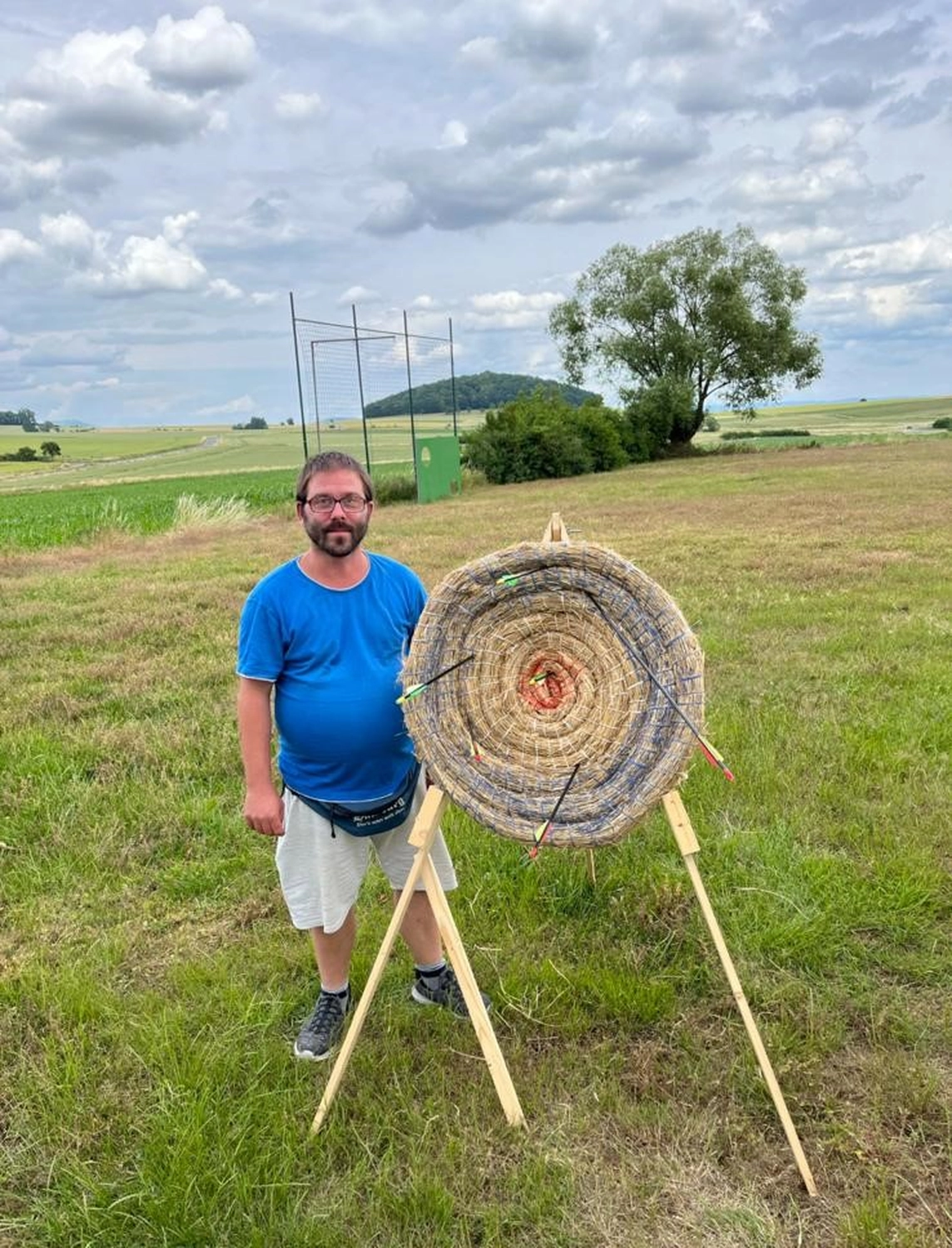 Soziale Teilhabe Kilian und Partner - sozialpädagogische Hilfe - eine Person, die Bogenschießen mit einer auf einem Holzständer montierten Strohzielscheibe auf einem Feld übt