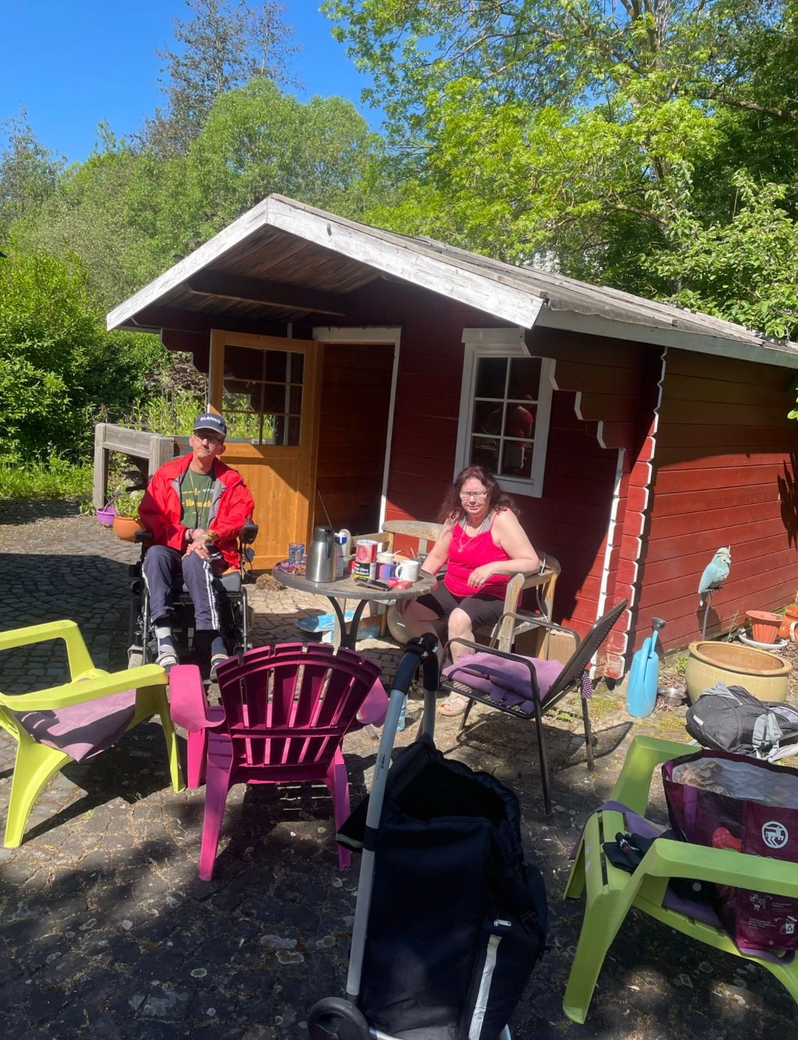 Soziale Teilhabe Kilian und Partner - sozialpädagogische Hilfe - Menschen sitzen vor einer kleinen, traditionellen roten Hütte
